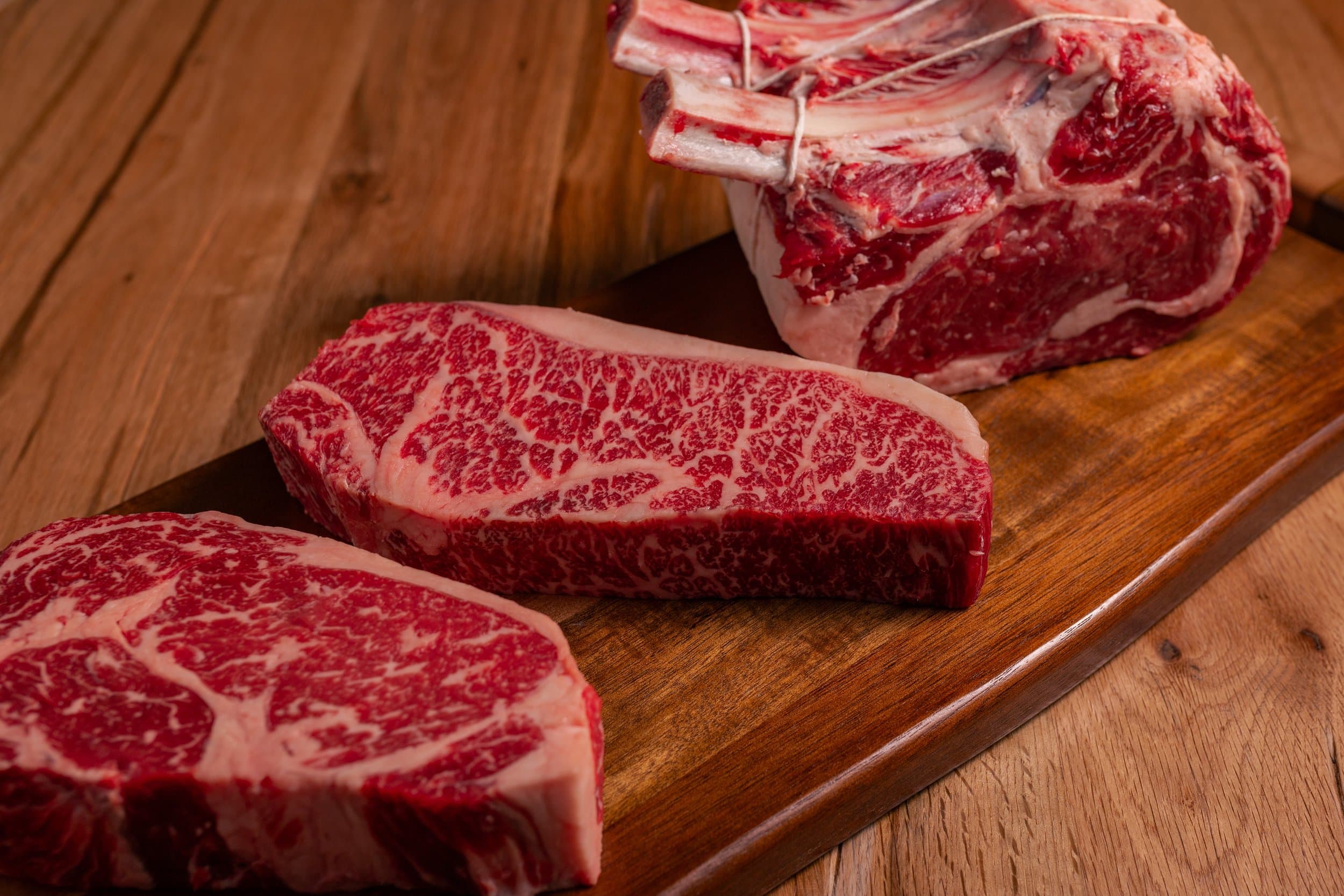 Ribeye and Wagyu steaks with a bone-in prime rib roast on a wooden cutting board